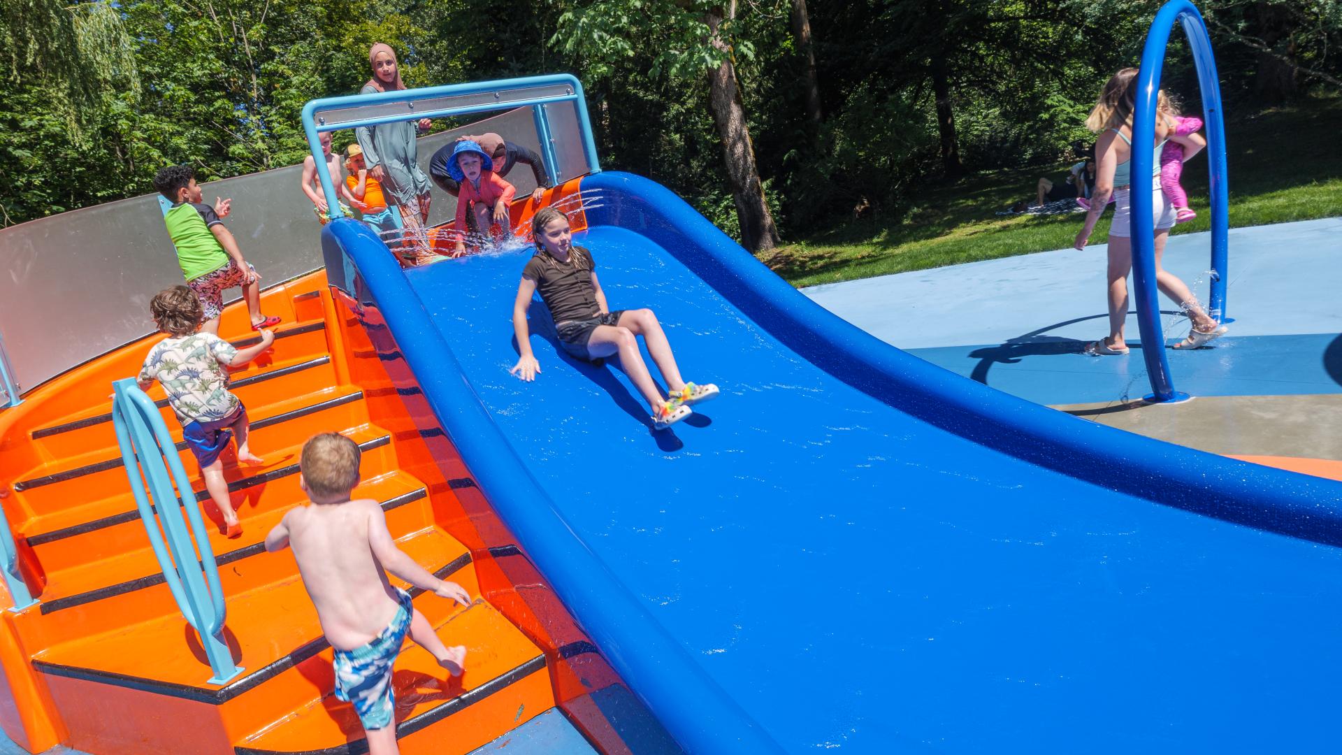 A short blue water slide with orange steps leading up and children playing